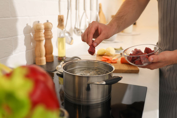 Man putting meat into pot to make bouillon in kitchen, closeup. Homemade recipe - Foto, immagini
