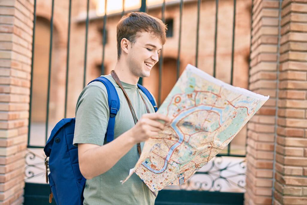 Jeune homme touristique caucasien souriant heureux tenant carte à la ville. - Photo, image