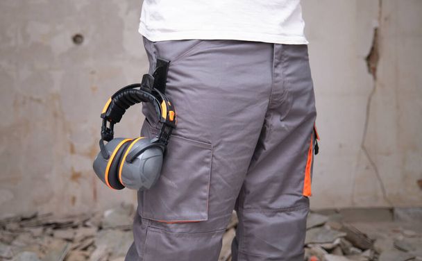 Construtor irreconhecível com proteção auditiva pendurada nas calças. Conceito de segurança no trabalho. - Foto, Imagem