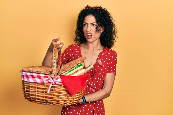 Молодая латинская девушка проводит пикник плетеной корзине с хлебом сердитый и сумасшедший кричать разочарованы и в ярости, кричать от гнева. гнев и агрессивная концепция.  - Фото, изображение