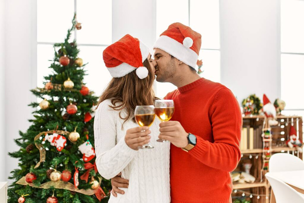 Junges hispanisches Paar mit Weihnachtsmütze stößt zu Hause mit Champagner an. - Foto, Bild