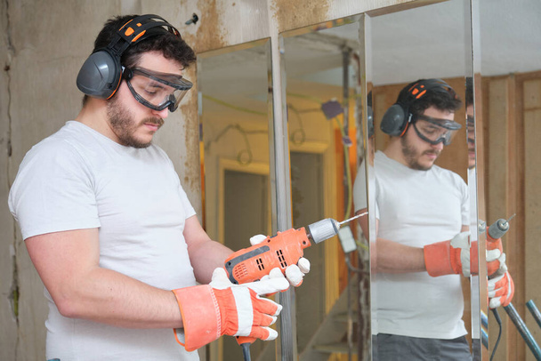 İnşaatçı inşaat alanında matkap ucu değiştiriyor. Güvenlik eldiveni, gözlük ve kulaklık takan inşaat işçisi.. - Fotoğraf, Görsel
