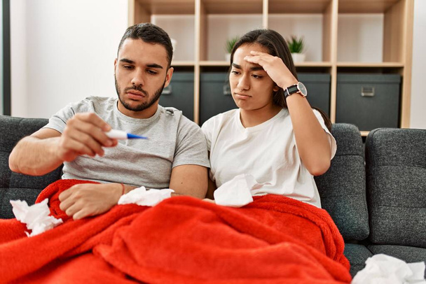 Junges lateinisch krankes Paar misst Temperatur mit Thermometer zu Hause. - Foto, Bild