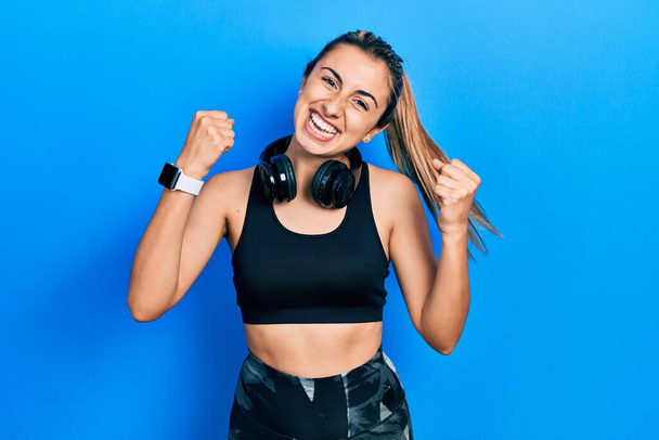 Beautiful hispanic woman wearing gym clothes and using headphones celebrating surprised and amazed for success with arms raised and open eyes. winner concept.  - Photo, Image