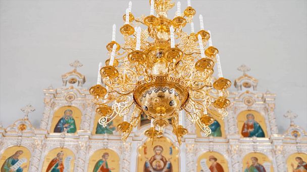 Keresztény ortodox templom belső fehér és arany színekben. Videó. Csillár mesterséges gyertyákkal a templomban ikonosztázissal. - Fotó, kép