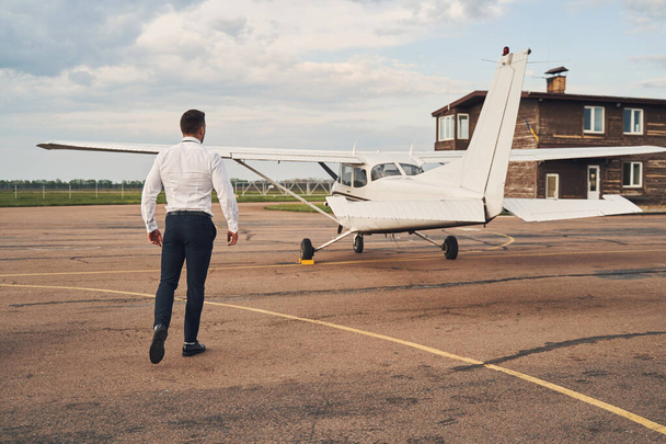 Stylish young man walking towards aircraft at airdrome - Zdjęcie, obraz