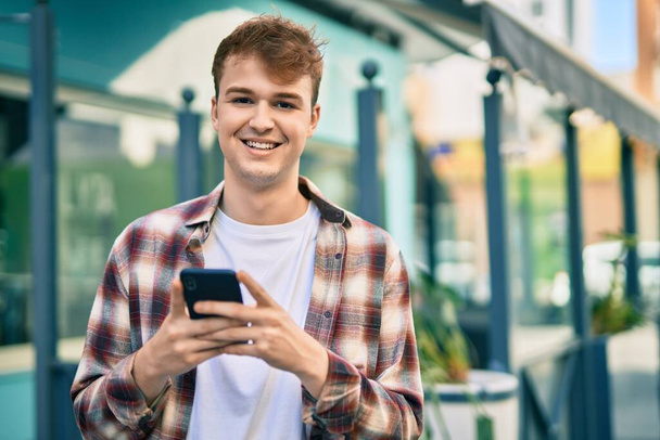 Молодой кавказский мужчина улыбается счастливо, используя смартфон в городе. - Фото, изображение