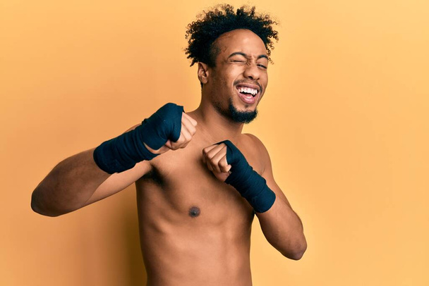 Jonge Afrikaans-Amerikaanse man met baard draagt boksbescherming knipogen naar de camera met sexy uitdrukking, vrolijk en gelukkig gezicht.  - Foto, afbeelding