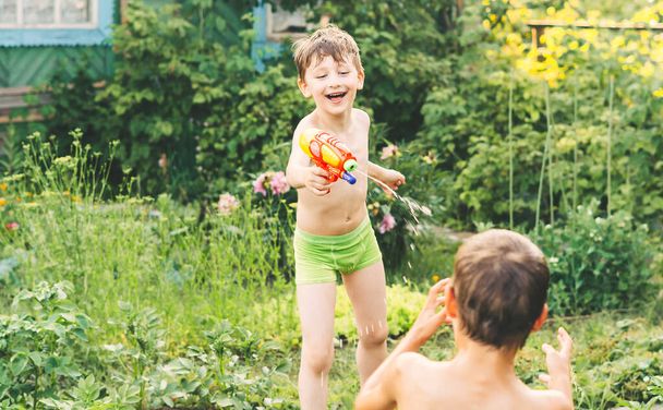 Dwóch małych chłopców bawiących się pistoletami na wodę w upalny letni dzień. Słodkie dzieci bawiące się wodą na podwórku. Zabawne gry letnie dla dzieci. Bracia walczący na świeżym powietrzu - Zdjęcie, obraz