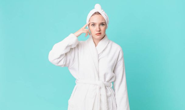 blond pretty woman feeling confused and puzzled, showing you are insane and wearing bathrobe - Foto, Bild