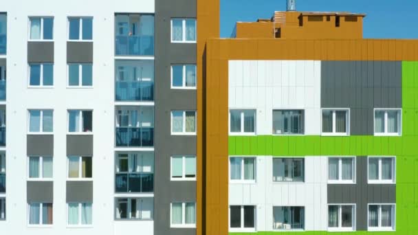 Αεροφωτογραφία της κατοικημένης περιοχής της πόλης με νέα σύγχρονα, πολύχρωμα, πολυώροφα κτίρια. Βίντεο. Έννοια της αρχιτεκτονικής, που φέρουν κατά μήκος των νέων σπιτιών σε φωτεινό μπλε φόντο του ουρανού. - Πλάνα, βίντεο