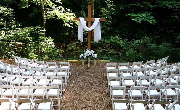 Un ambiente esterno di una cerimonia nuziale con sedie bianche e un panno bianco su una croce - Foto, immagini
