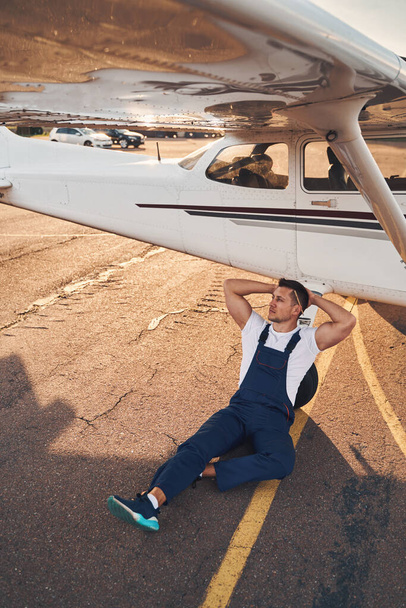 Красивый молодой человек отдыхает возле самолета на аэродроме - Фото, изображение