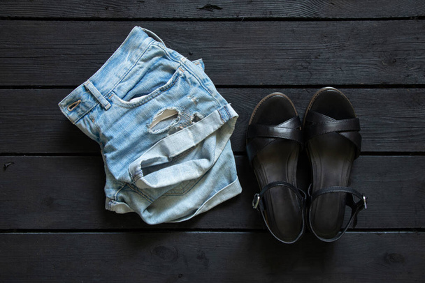 damesshorts en zomersandalen op een zwarte houten ondergrond, mode, dameskleding en schoenen - Foto, afbeelding