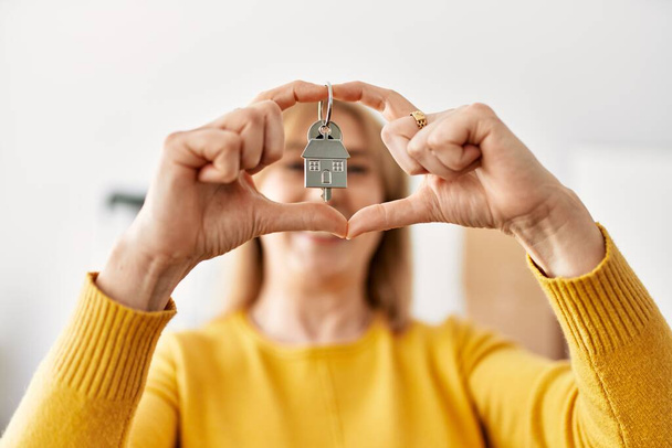 блондинка среднего возраста делает сердечный знак с руками и держит ключ от нового дома. - Фото, изображение
