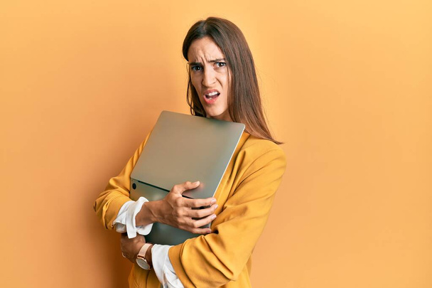 Young beautiful woman holding laptop in shock face, looking skeptical and sarcastic, surprised with open mouth  - Photo, Image
