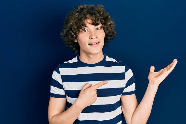 Handsome young man wearing casual striped t shirt amazed and smiling to the camera while presenting with hand and pointing with finger.  - Photo, Image
