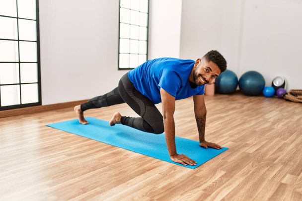 Handsome hispanic man doing exercise and stretching on yoga mat, practicing flexibility and training at the gym - Foto, Bild