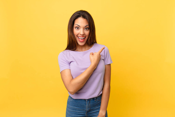 young hispanic woman looking excited and surprised pointing to the side - Foto, Imagen