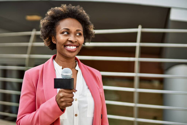 記者マイクを持っている若いアフリカ系アメリカ人女性ジャーナリストは、テレビのニュースのためにカメラに話して笑顔 - 写真・画像