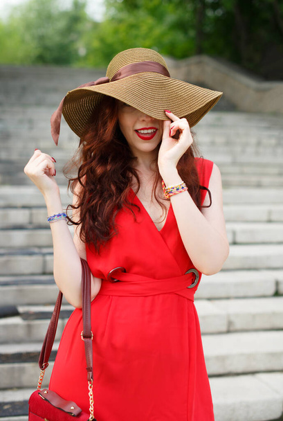 A happy young woman, in a wide hat, poses in a park in summer - Fotoğraf, Görsel
