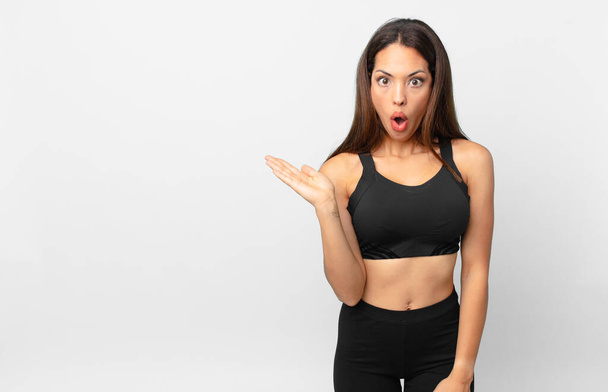 young hispanic woman looking surprised and shocked, with jaw dropped holding an object. fitness concept - Fotó, kép