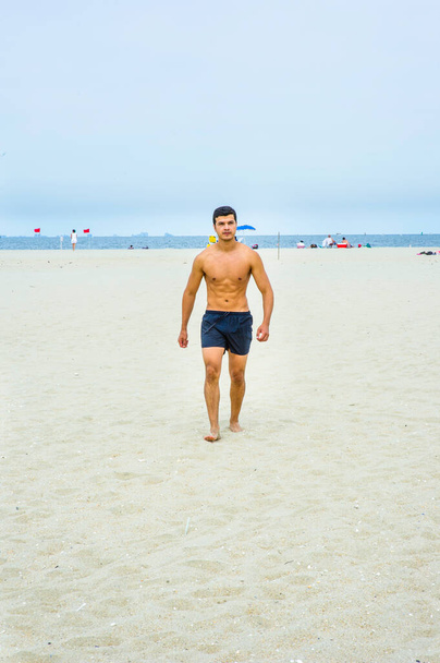 Een jonge man, half naakt, loopt op het strand. - Foto, afbeelding