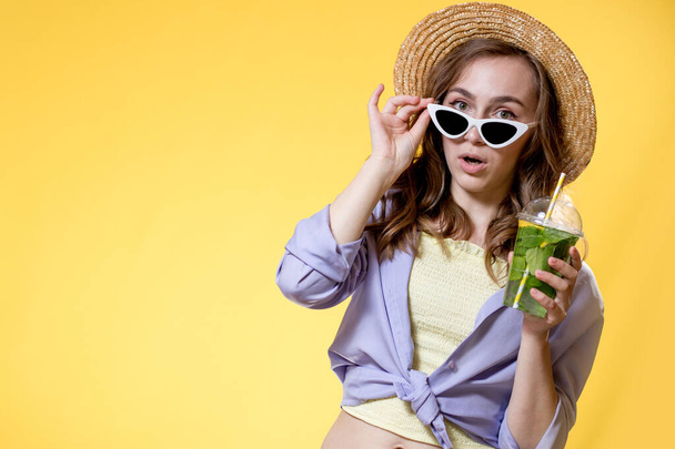 Surprised Woman Drink Mojito cocktail From Plastic Cup Over Yellow Studio Background - 写真・画像