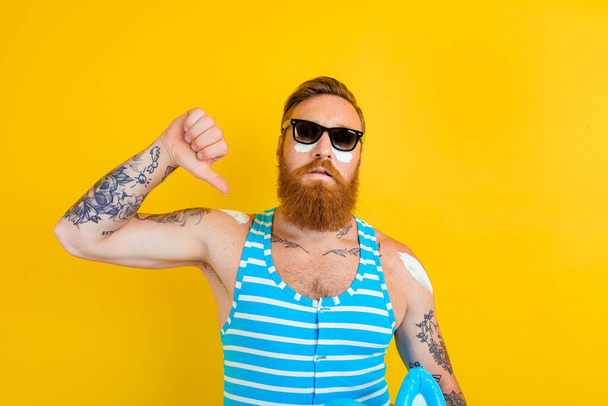 man with tattoos and swimsuit puts on sunscreen - Photo, Image