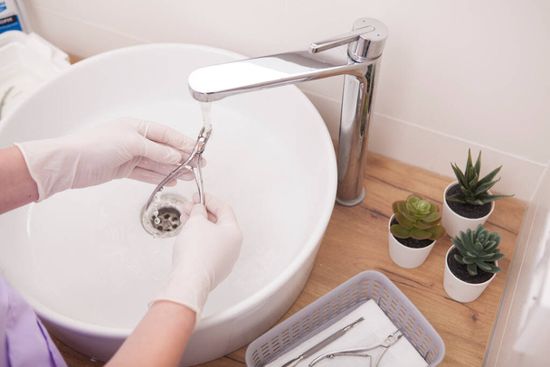 Unrecognizable manicurist wearing rubber gloves, washing nippers in the sink - Foto, Imagen