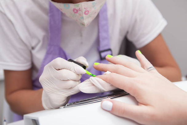 Close up of manicurist doing yellow neon nails for client - Фото, зображення