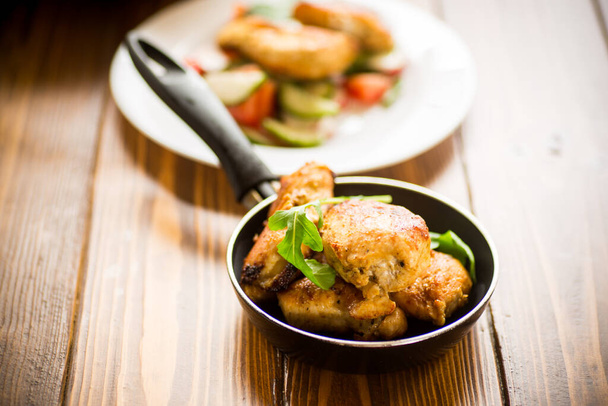 fried pieces of chicken fillet in a pan on a wooden table - Foto, afbeelding