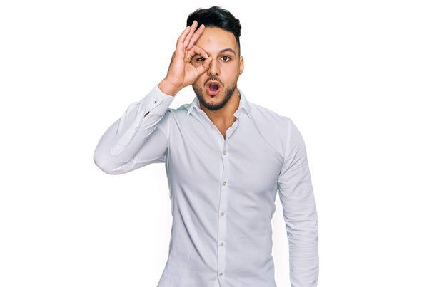 Young arab man wearing casual clothes doing ok gesture shocked with surprised face, eye looking through fingers. unbelieving expression.  - Foto, afbeelding