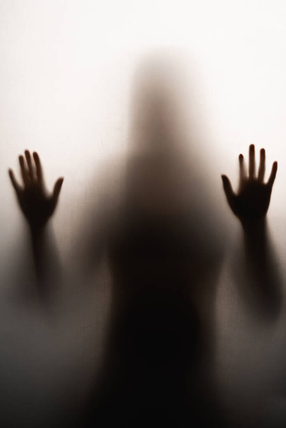 zacht vrouwelijk silhouet op een donkere achtergrond met duidelijke handen op het glas - Foto, afbeelding
