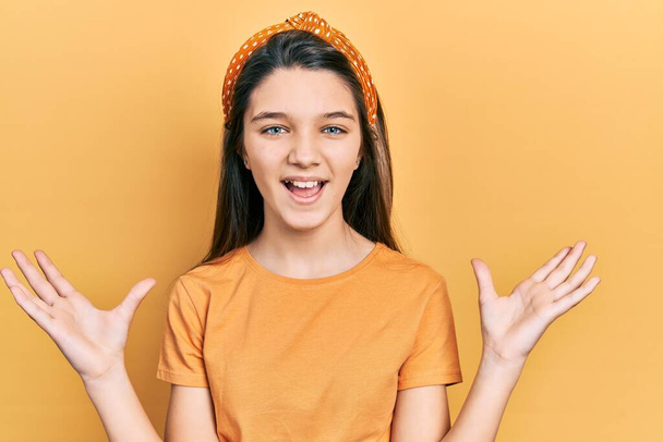 Fiatal barna lány visel alkalmi narancssárga póló ünnepli őrült és őrült siker karok emelt és csukott szemmel sikoltozó izgatott. győztes koncepció  - Fotó, kép