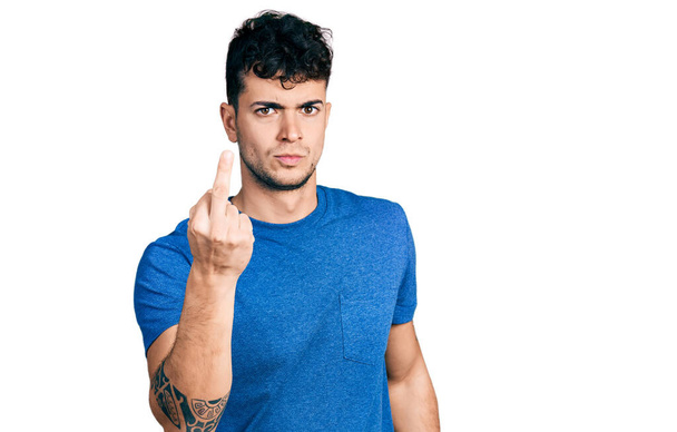 Молодой латиноамериканец в обычной футболке, показывающий средний палец, невежливый и грубый...  - Фото, изображение
