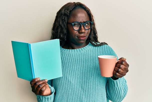アフリカの若い女性の本を読んで、コーヒーのカップを飲んで懐疑的で緊張し、問題のために動揺を眉をひそめて。否定的な人.  - 写真・画像