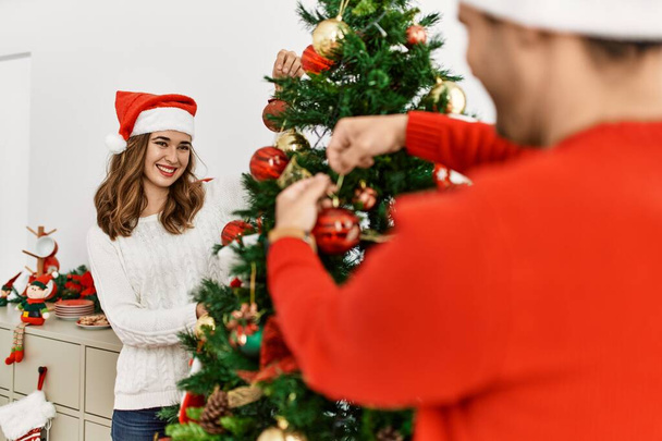 Joven pareja hispana decorando árbol de navidad en casa. - Foto, Imagen