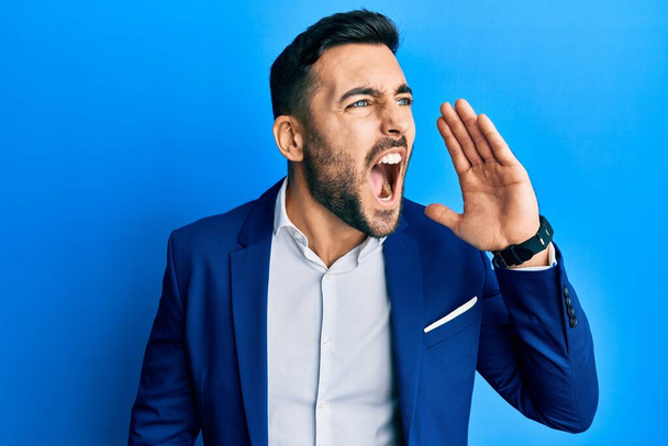 Young hispanic businessman wearing business jacket shouting and screaming loud to side with hand on mouth. communication concept.  - Photo, image
