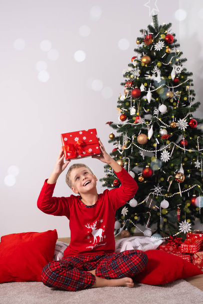 Portrait Of Excited Boy Holding Christmas Gift. Happy Child in Red Pajamas By Tree On Christmas - Foto, Imagen