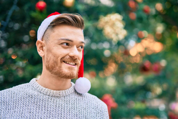 Young caucasian man smiling happy wearing christmas hat at the park. - Photo, Image