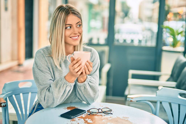 Jeune fille blonde buvant du café assis sur la table au café. - Photo, image