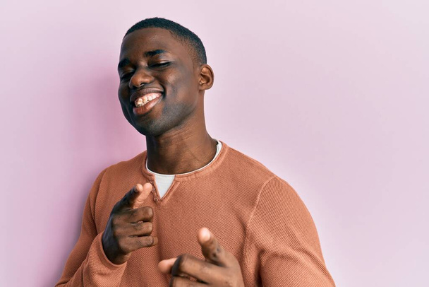 Молодий афроамериканець у повсякденному одязі вказує пальцями на камеру з щасливим і кумедним обличчям. добра енергія й трубопроводи.  - Фото, зображення