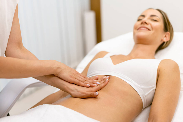 Middelbare leeftijd vrouw met een buik massage in een schoonheidssalon. - Foto, afbeelding