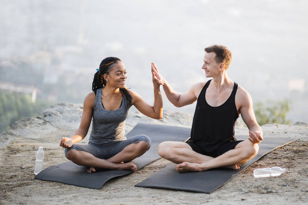 Sporty couple sitting on yoga mat and giving high five - Fotó, kép