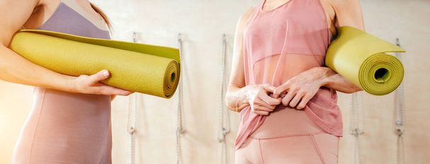 Woman wearing activewear standing in gym holding yoga mat ready to start fitness or yoga training. Concept of sports lifestyle. Yoga concept - Фото, изображение