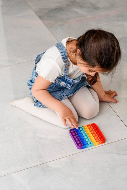 Niño sentado en el suelo jugando con el juguete Pop It Fidget. - Foto, Imagen