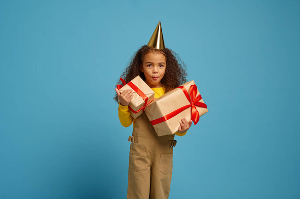 Funny little girl in cap holds birthday gift box - Φωτογραφία, εικόνα