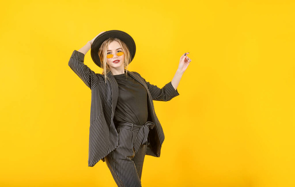 young blonde woman in a black jacket and hat smiles on a yellow background - Foto, Imagen