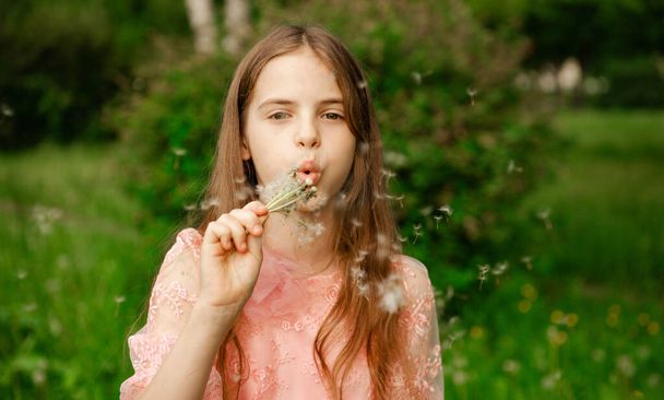 10 year old girl blows on a dandelion against a background of greenery - Фото, зображення